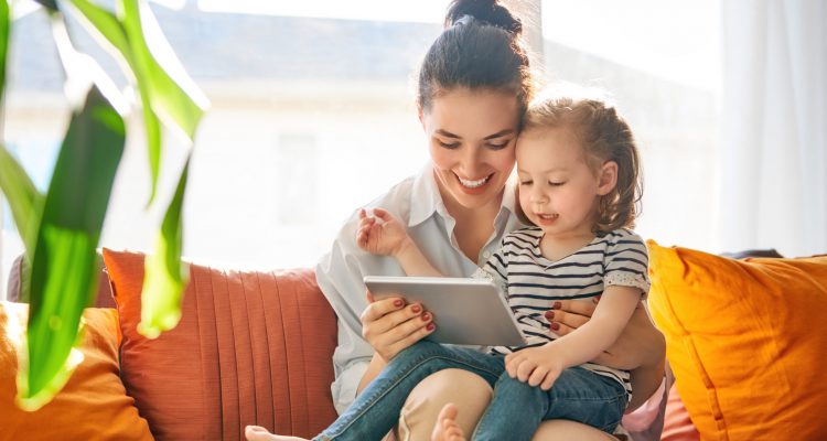 Happy loving family. Young mother and her daughter girl play in kids room. Funny mom and lovely child are having fun with tablet.